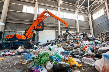 Excavator grabs trash in warehouse of waste processing plant
