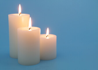 Fototapeta na wymiar Three white scented candles melting on blue background. Space for text.