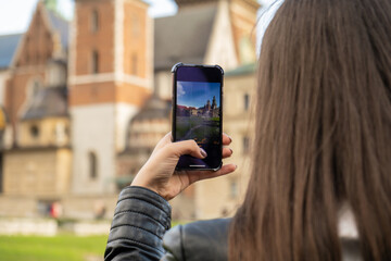 Female traveler in historical places looks around courtyard of landmark and shoots short video on phone. Tourist photographs historic place on sunny day. Unrecognizable woman Tourism and blogging