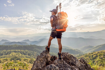Young male hiker with backpack enjoying sunrise on top mountain park.