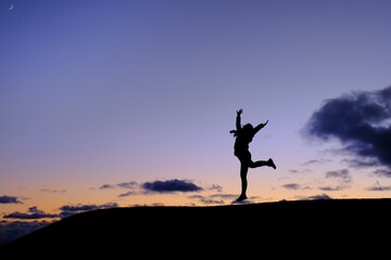 A silhouette of a woman in gym uniform jumping on top of a hill in celebration after completing her...