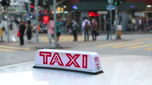 A taxi sign sits on the hood of the vehicle as pedestrians walk through a zebra crossing in the background.