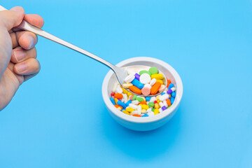 A mortar is placed on a blue background and filled with colorful pills capsules, a spoon and an empty space to use as a copyspace. human hand is floating with a spoon.