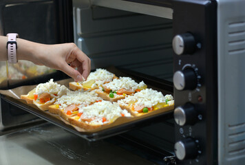 home cooking With slices of bread, topped with cheese, sausage, ham, beans and carrots, ready to bake in the electric oven.