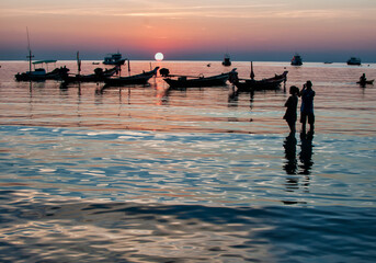 Fototapeta premium An idyllic sunset with a silhouette of a woman and a man on the beach in Koh Chang