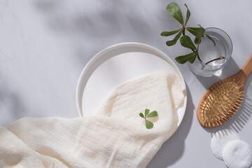 Obraz na płótnie Canvas A round dish decorated with a white towel, cotton pads, wooden brush and a glass vase with tree branch. Empty space for natural beauty product advertising