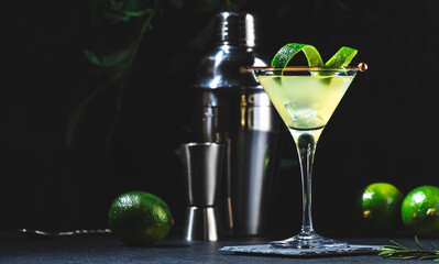 Gimlet alcoholic cocktail with dry gin, liqueur, lime juice and ice in glass garnished with lime zest. Black background