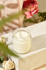 Fototapeta na wymiar Composition with aromatic candle in jar on concrete podium. Mockup soy wax candle in natural style with flower. Scented handmade candle with wick. Handmade spa product from soy wax in glass.