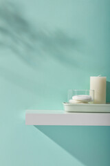 Minimal concept with scented candles and remove makeup cotton in rectangle tray on white pedestal. Natural shadow leaves on blue wall. Empty space for display product. Front view, copy space.
