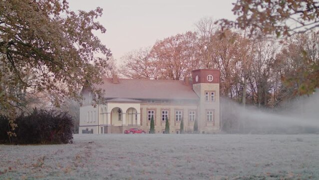 Establishing cinematic view to a luxury villa with a sleek red sports car parked in front. Frosty autumn morning and fog before sunrise.