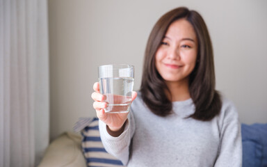 Portrait image of a young woman holding and showing a glass of water