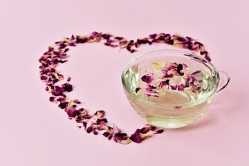 Fototapeta premium dried rose petals place like a heart, hot rose tea in glass cup