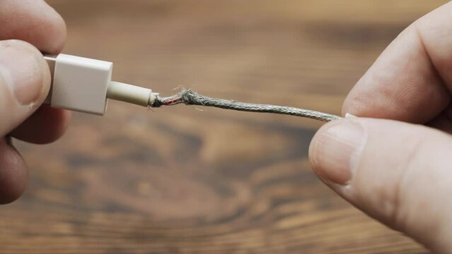 A man examines a faulty USB charger cable with damaged wire insulation. Close-up.