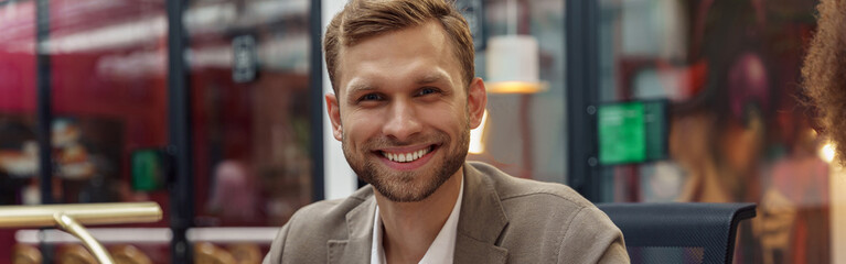 Smiling businessman sitting on meeting in modern office and looking at camera