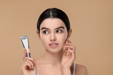 Teenage girl holding tube with foundation on beige background