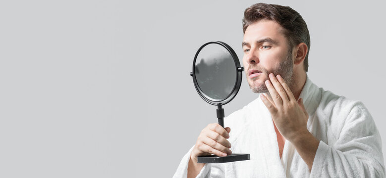 Millennial Hispanic Man Looking In Mirror In Bathroom, Facial Skin And Stubble. Male Beauty Care Product. Skincare, Home Spa. Beauty Portrait Of A Beautiful Man. Spa, Moisturizing Nourishing Creme.