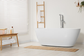 Fototapeta na wymiar Stylish bathroom interior with ceramic tub, care products and terry towels on table