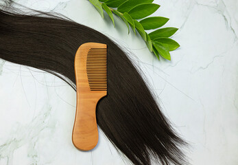 Hair care wooden comb on a long strand of black hair on a white background. Tools from biological...