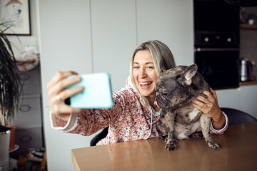 Happy pretty blonde in homemade clothes is happy to take selfie with her beloved French bulldog. Owners and pets. 