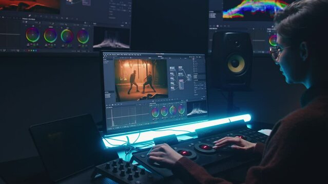 Female editor uses color grading control panel, edits video, makes movie color correction on computer and tablet in studio. Film footage and RGB wheels on monitor. Big screens with program interface.