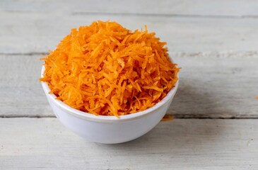 Closeup of Grated Carrot in a White Bowl Isolate on White Wooden Background