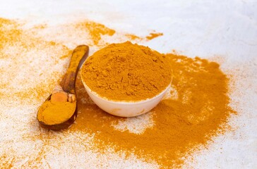 Turmeric Powder in a White Bowl with Turmeric Root and Powder in a Wooden Spoon Isolated on White Background with Copy Space