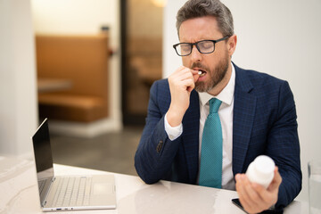 Sad man got migraine touches her head because of pain. Man manager with strong headache working on laptop. Man taking a medicine pill from headache migraine.