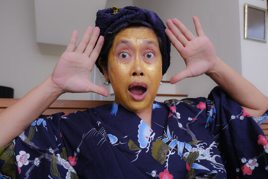A woman with a beauty mask on her face with open arms beside her head; surprised.