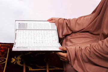 Islamic moslem woman praying Koran or Quran on praying carpet sajadah wearing traditional dress