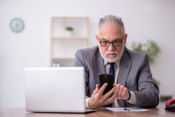 Old male employee speaking by phone at workplace