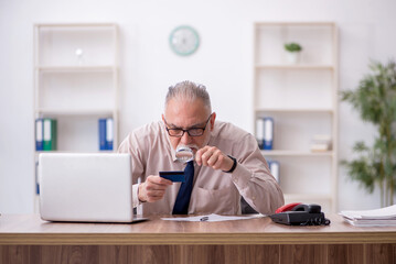 Old male employee holding credit card at workplace