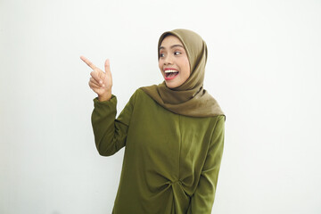 Beautiful young Asian Muslim woman wearing green dress and hijab pointing finger at free space place for an advertisement isolated on white background. People religious Islamic lifestyle concept