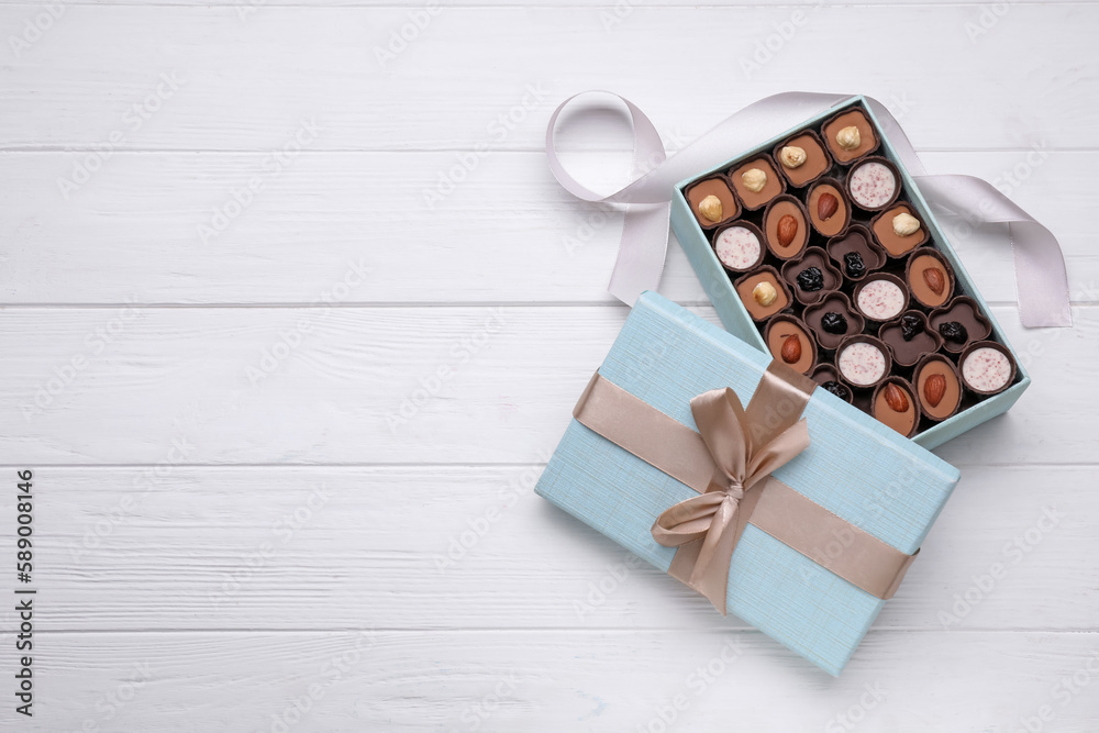 Poster Open box of delicious chocolate candies and color ribbon on white wooden table. flat lay. Space for text