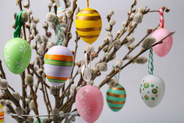 Fototapeta na wymiar Vase with beautiful willow branches and painted Easter eggs on light grey background, closeup