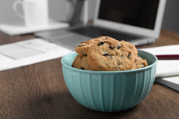 Bowl with chocolate chip cookies on wooden table in office, closeup