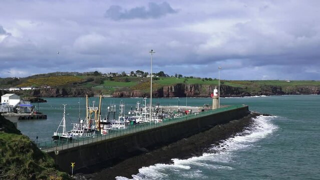 Dunmore East Fishing Harbour trawlers safe from the approaching winter storm with waves starting to break on the sea wall