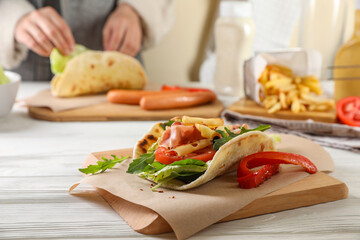 Woman cooking delicious pita wrap with jamon, cheese and vegetables at wooden table. Focus on dish