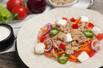Delicious tortilla with tuna, vegetables and cheese on wooden table, closeup. Cooking shawarma