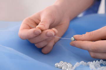 Dressmaker stringing bead on thread at light blue fabric in atelier, closeup