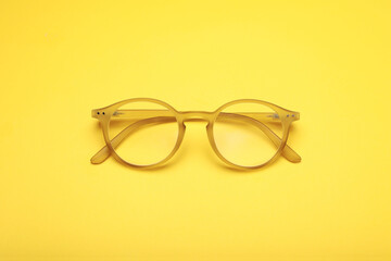 Glasses with corrective lenses on yellow background, top view