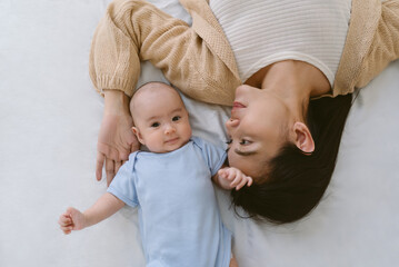 Beautiful young Asian mother and her adorable newborn baby lying on white bed at home. Newborn...