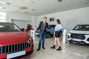 Caucasian female salesperson giving consultation to male customer in modern car showroom.