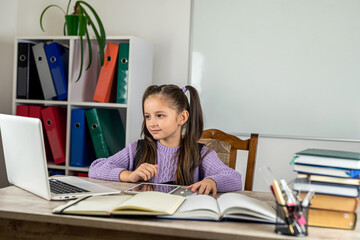 Portrait of a beautiful girl in the classroom at a desk with books and a computer.