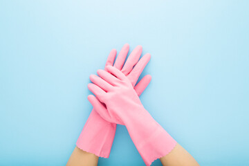 Young adult woman hands in pink rubber protective gloves on light blue table background. Closeup. Point of view shot. Top down view.