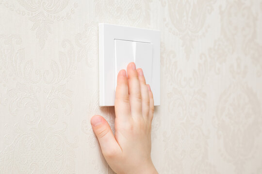 Little Child Hand Pressing White Plastic Light Switch Buttons At Wall In Room. Turn On Or Turn Off Lighting. Closeup. Energy Saving At Home. Side View.