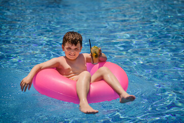  Child is smiling and drinking cocktail in the swimming pool..