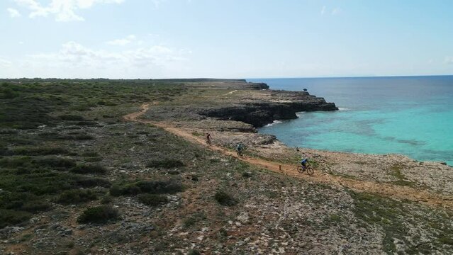 Athletes race along the coastline of Menorca, Spain. Rocky terrain lines the clifftops.