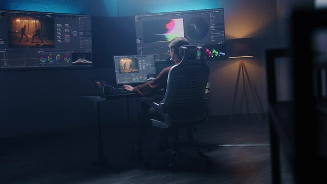 Female film editor or colorist does color grading on computer in modern studio. Big monitors with RGB colour correction graphic bar and program interface on the wall. Video post production. Handheld.