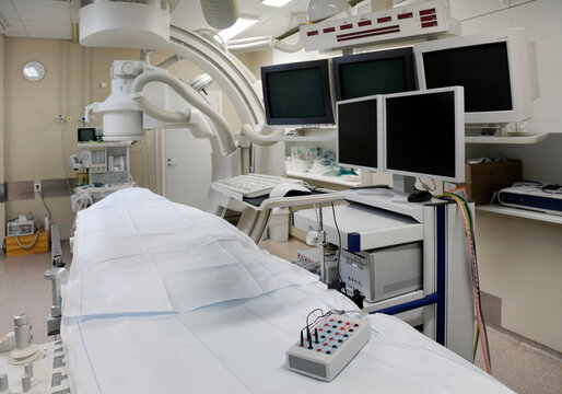 A modern hospital room, a large portable mobile scanning machine with curved shaped arms and banks of screens for medical imaging. 