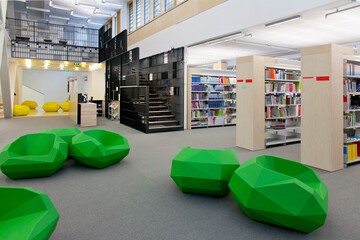 A healthcare college library with open spaces, green chairs and book stacks. A modern light and airy building. 
